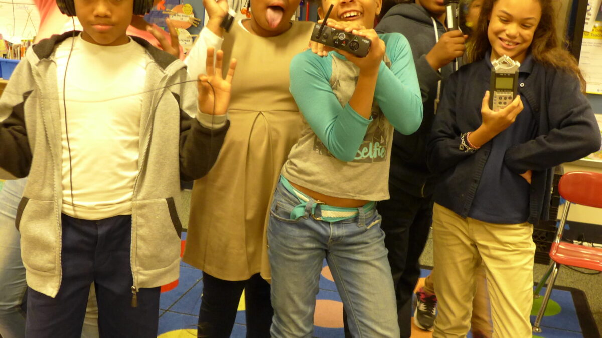 Six youth wearing headphones posing with portable recorders in a classroom
