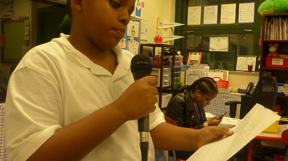 A youth holding a piece of paper and a microphone in a classroom