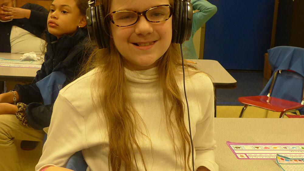 A youth wearing headphones smiling at the camera in a classroom