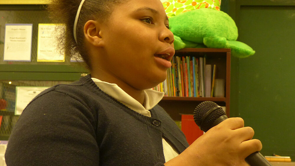 A youth speaking into a microphone in a classroom