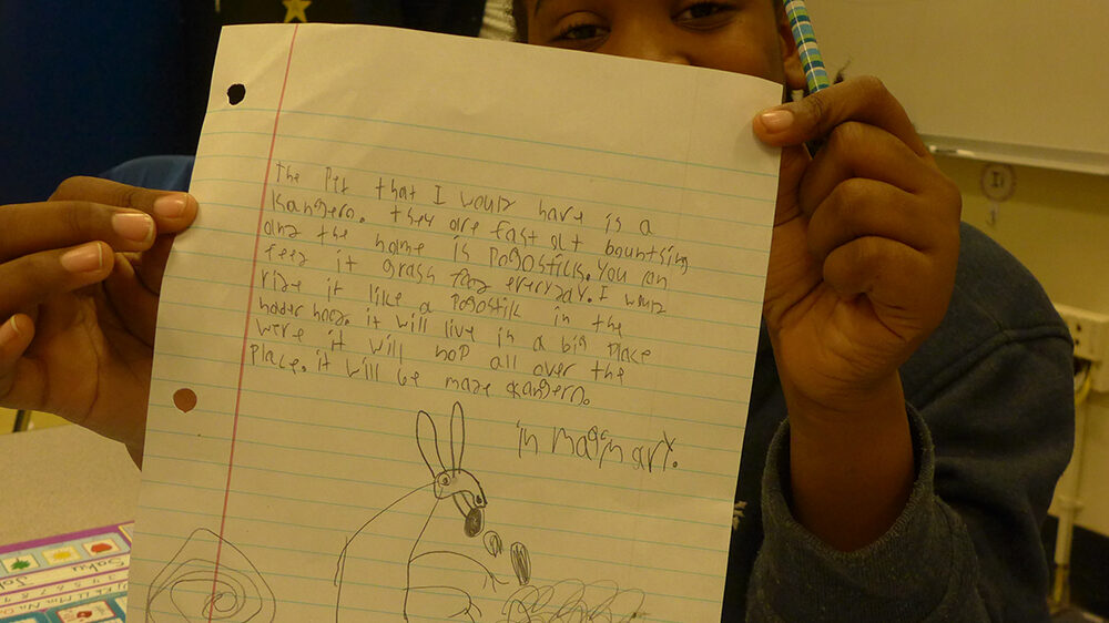 A youth holding a piece of notebook paper up to the camera in a classroom