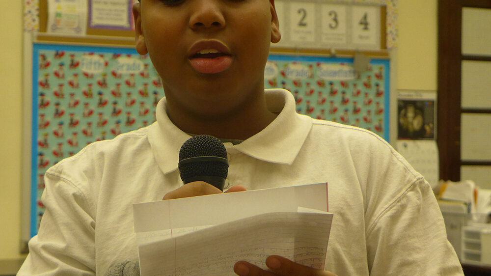 A youth reading a piece of paper into a microphone in a classroom