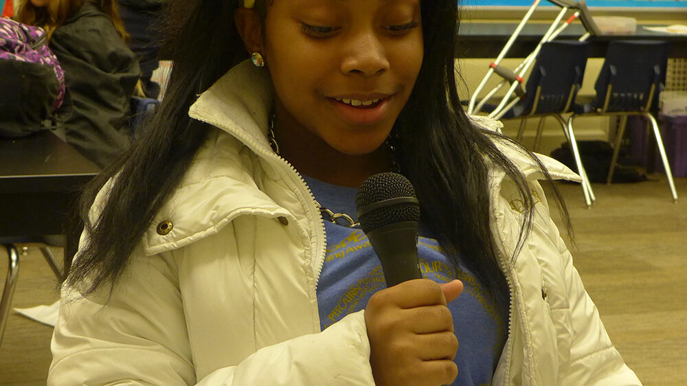 A youth holding and speaking into a microphone in a classroom