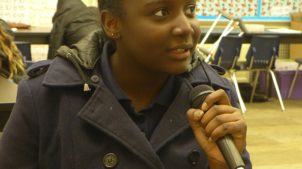 A youth holding and speaking into a microphone in a classroom
