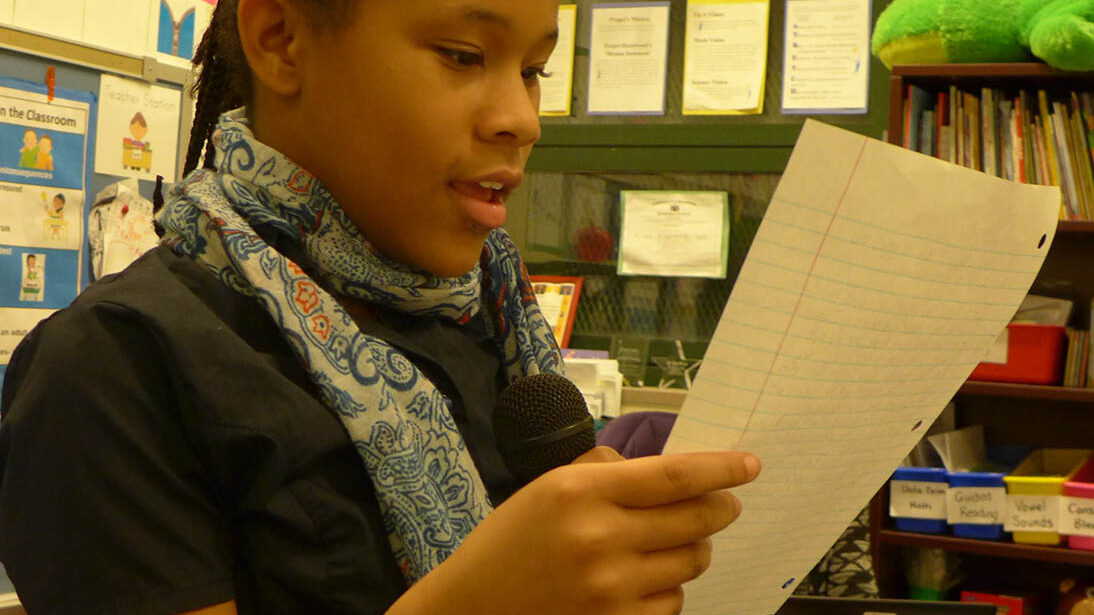 A youth holding and reading a piece of paper in a classroom