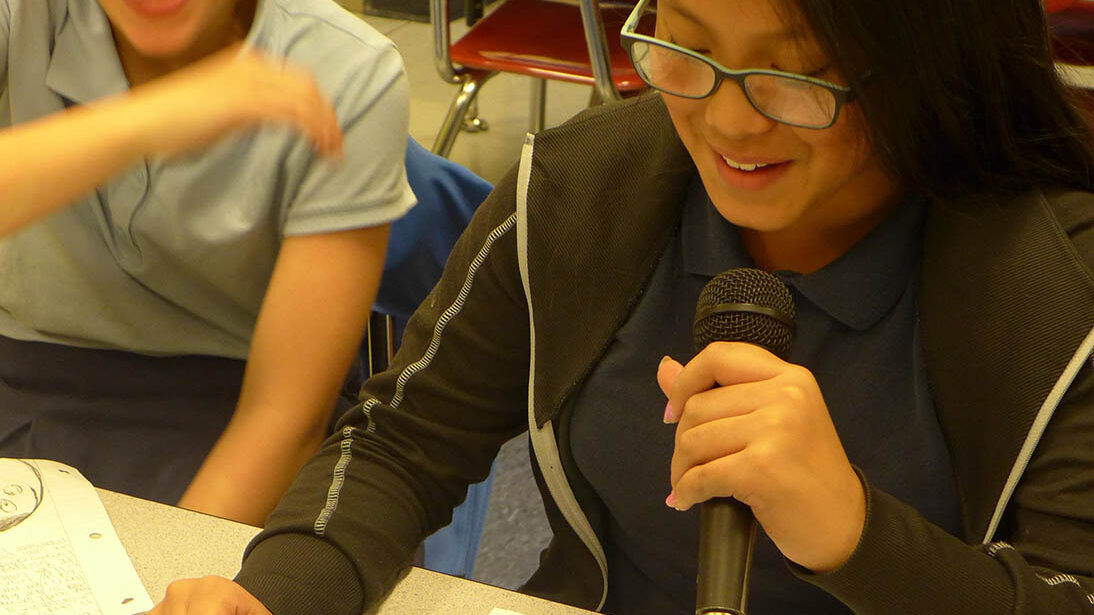 Two youth laughing in a classroom, one holding a microphone