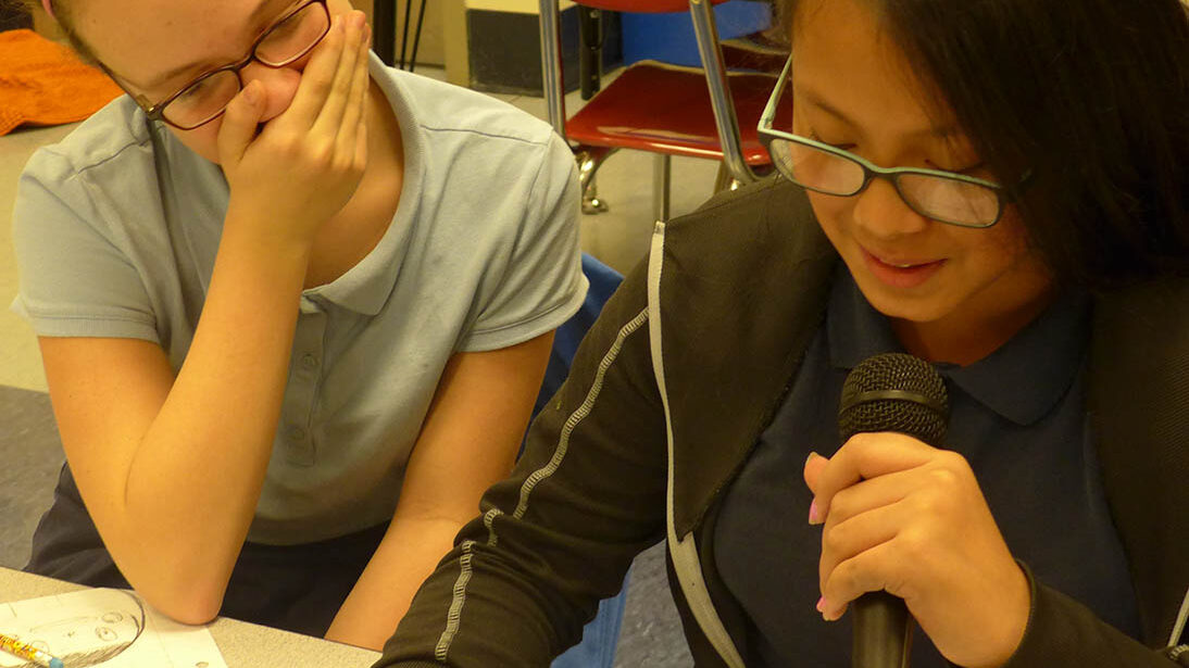 Two youth laughing in a classroom, one holding a microphone