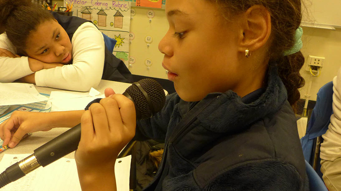 A youth holding and speaking into a microphone in a classroom
