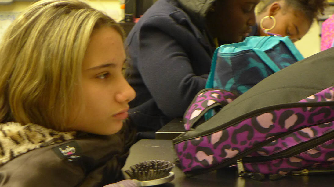 Three youth sitting behind their backpacks in a classroom