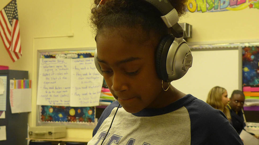 A youth wearing headphones looking down in a classroom