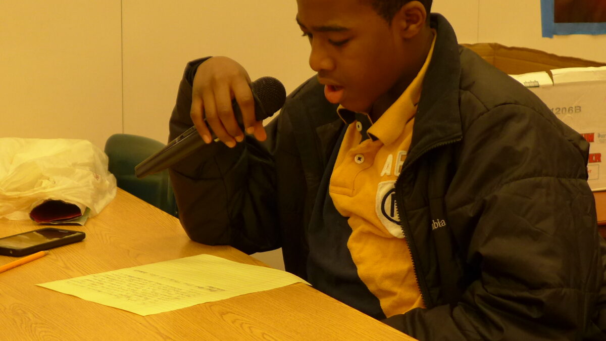 A teen looking down at a piece of paper on a table in a classroom
