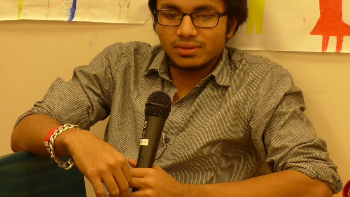 A teen holding a microphone in the corner of a classroom