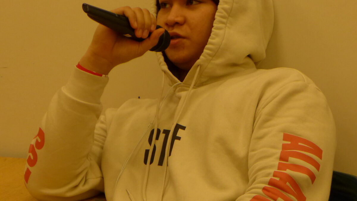 A teen holding and speaking into a microphone in a classroom