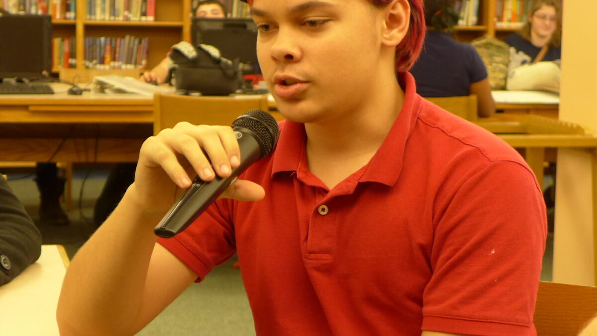 A teen holding and speaking into a microphone in a library