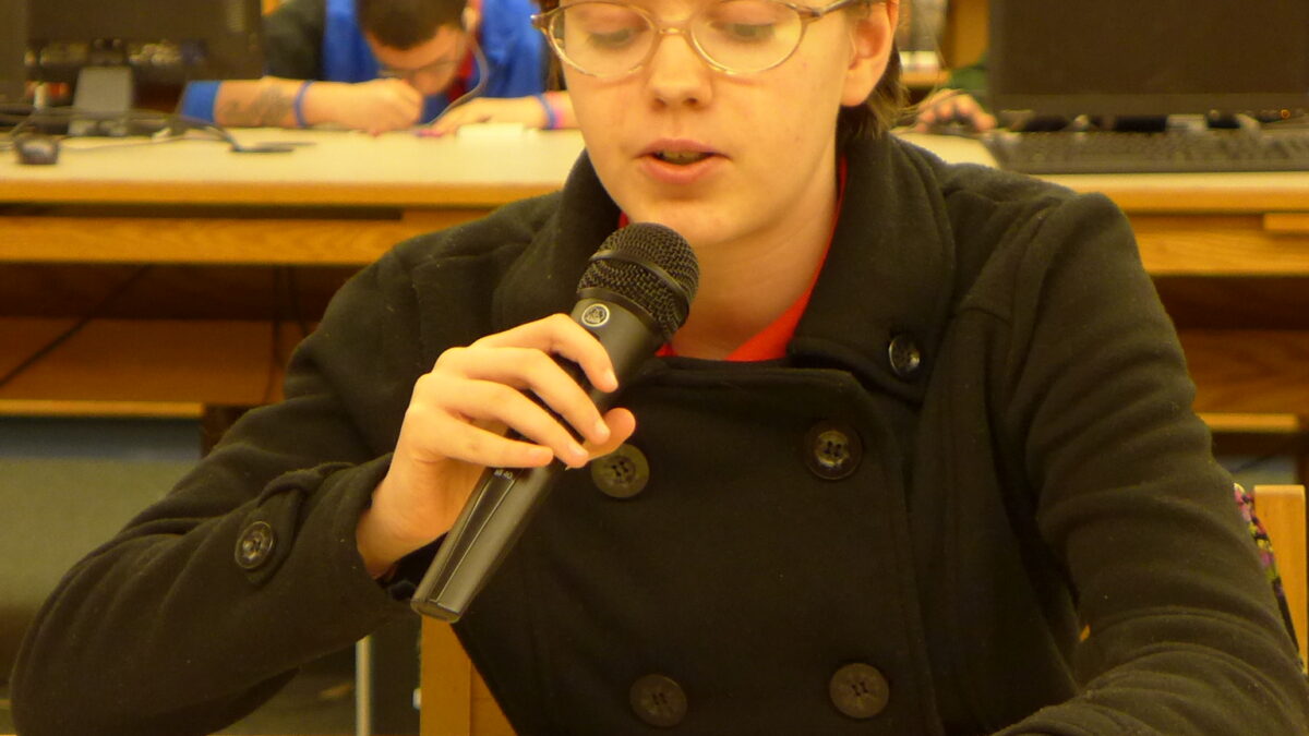 A teen holding and speaking into a microphone in a library