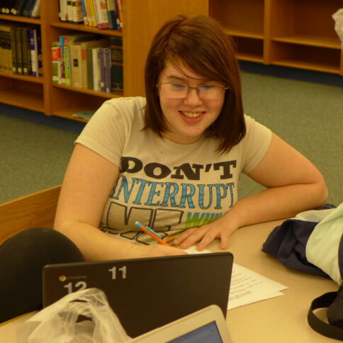 A youth looking at a laptop computer and writing on a piece of paper