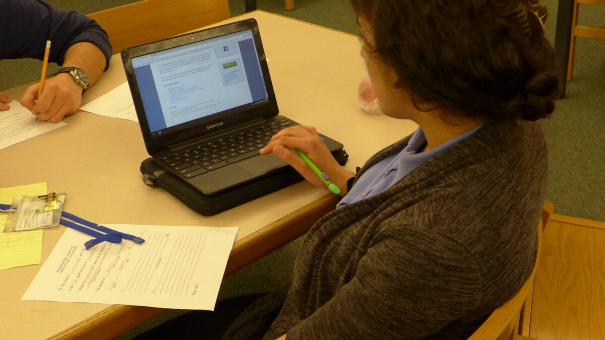 A youth sitting with a piece of paper and a laptop computer