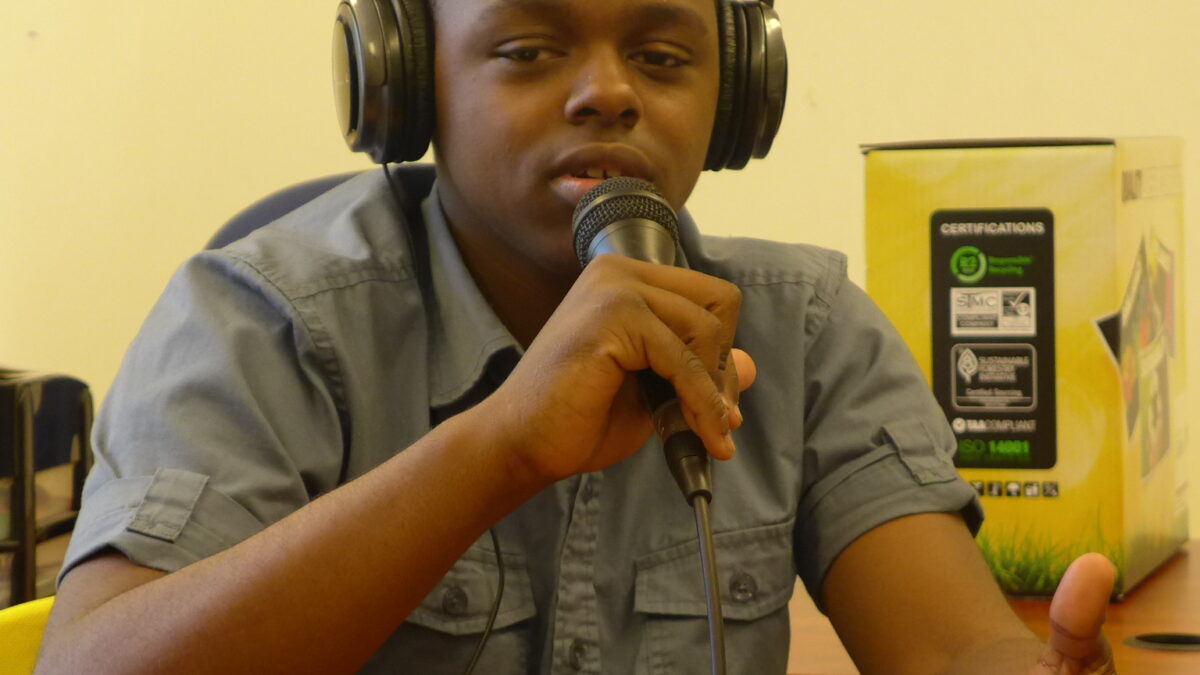 A youth wearing headphones speaking into a microphone and gesturing with their hand.