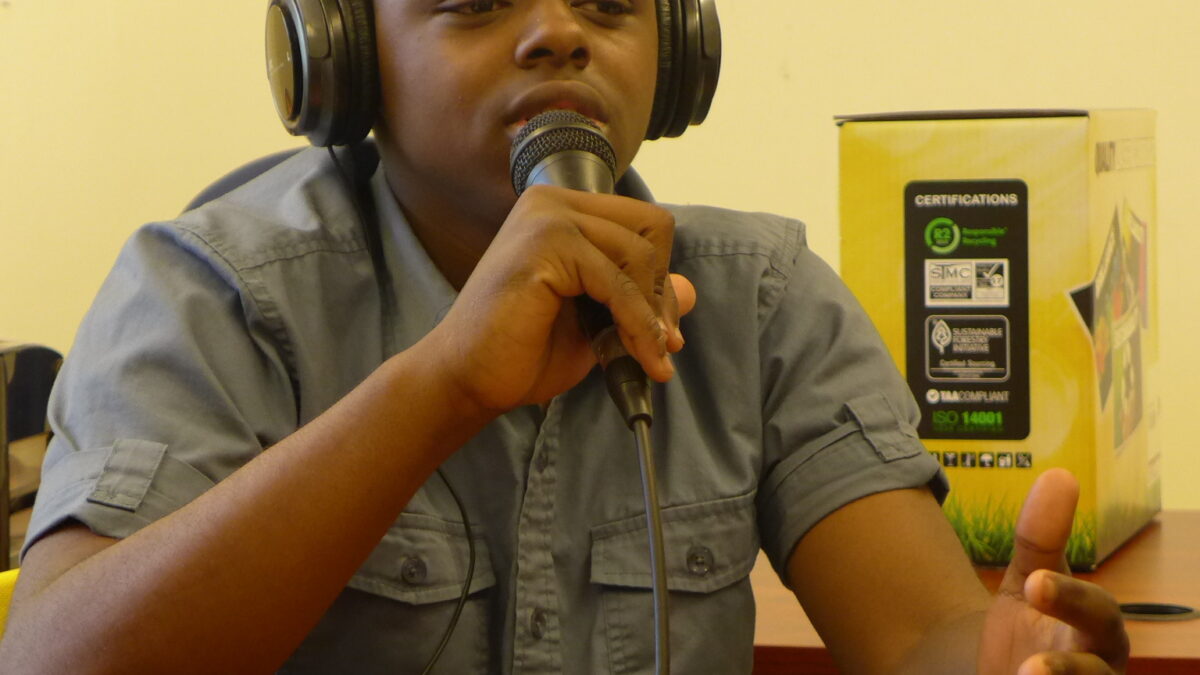 A youth wearing headphones speaking into a microphone and gesturing with their hand.