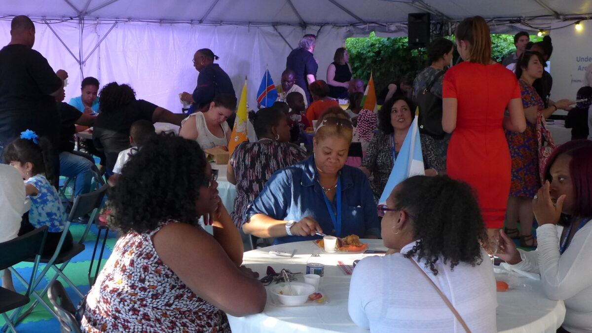 A large crowd gathered in a large white tent with blue piece of paper hanging from the ceiling