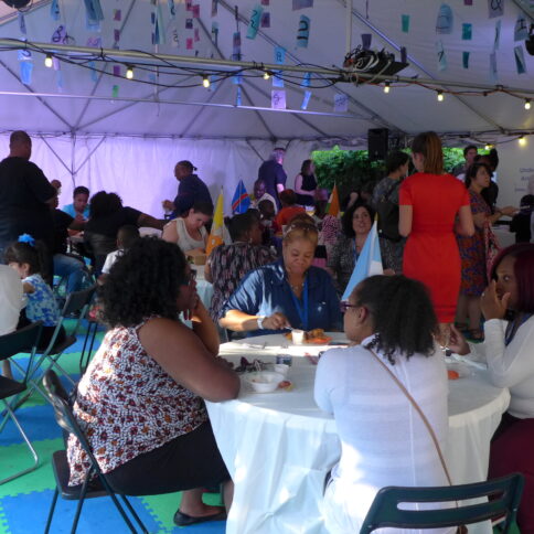 A large crowd gathered in a large white tent with blue piece of paper hanging from the ceiling