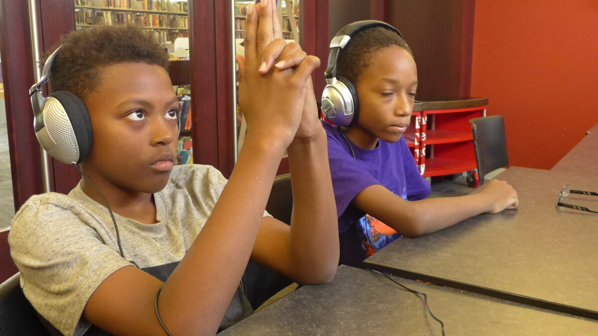 Two youth wearing headphones, one making a gun with their fingers
