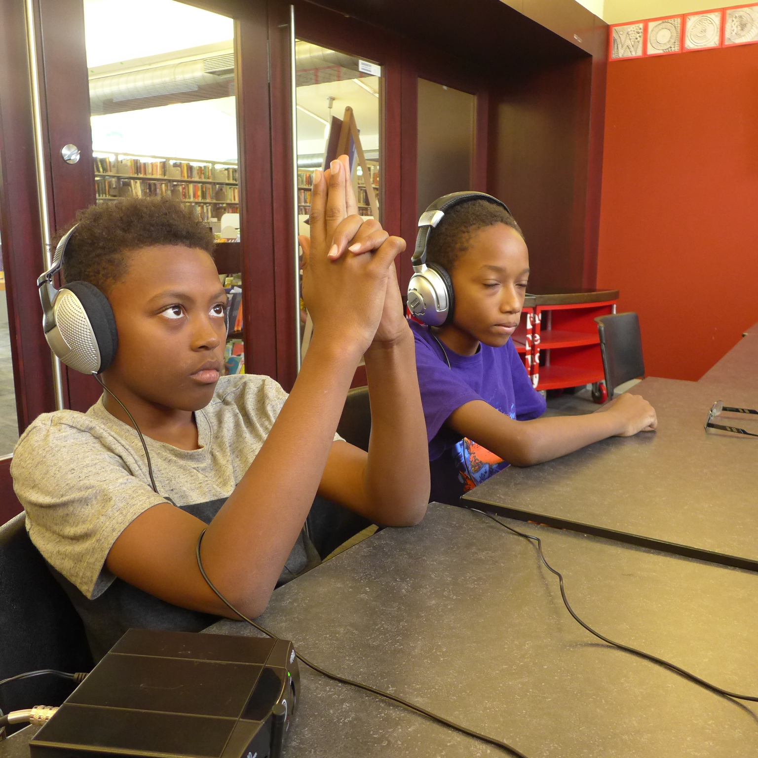 Two youth wearing headphones, one making a gun with their fingers