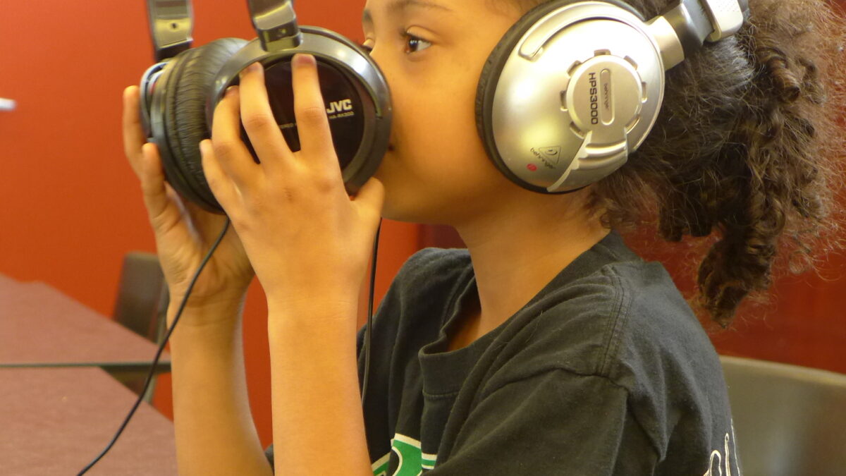 A youth wearing headphones holding another pair of headphones