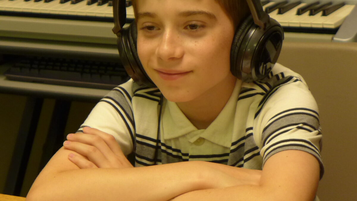 A youth wearing headphones smiling and folding their arms on a wooden table