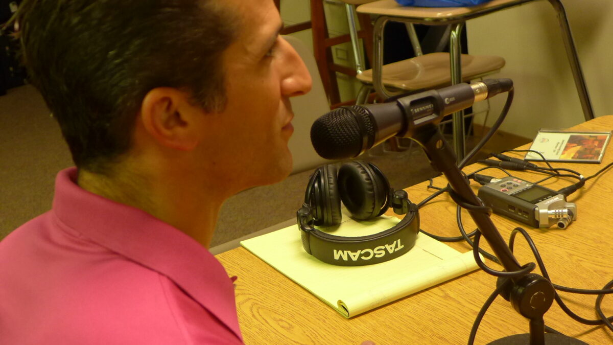 An adult speaking into a microphone connected to a portable recorder on a wooden table
