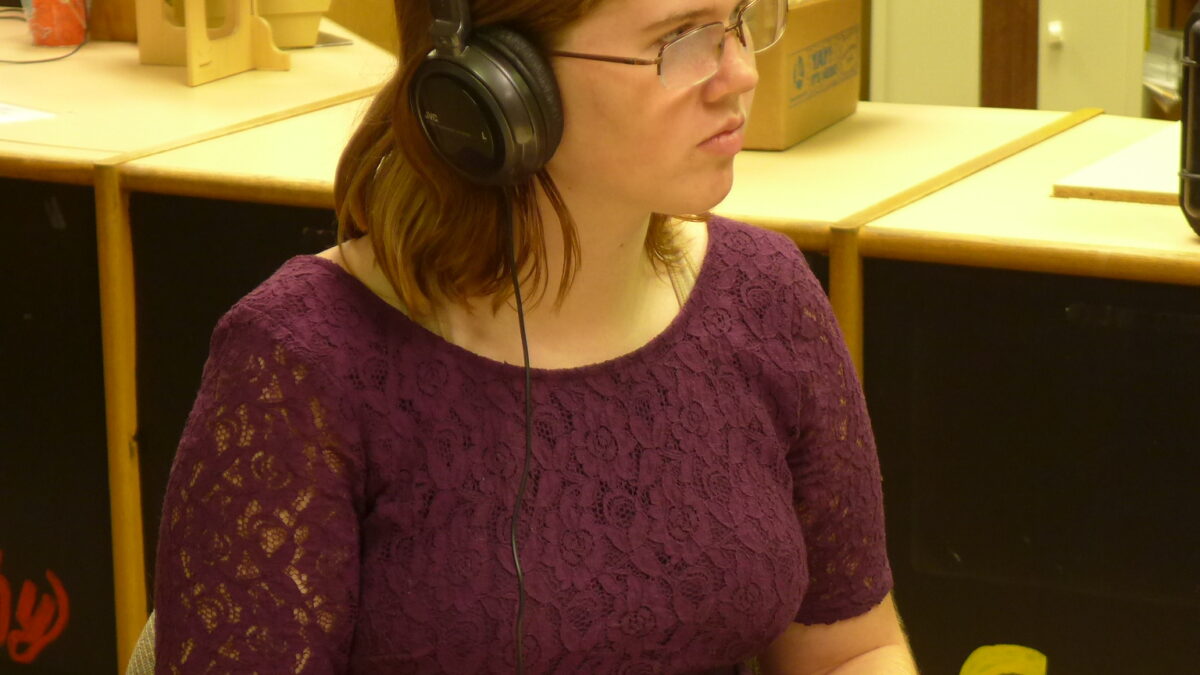 An adult wearing headphones writing onto a clipboard