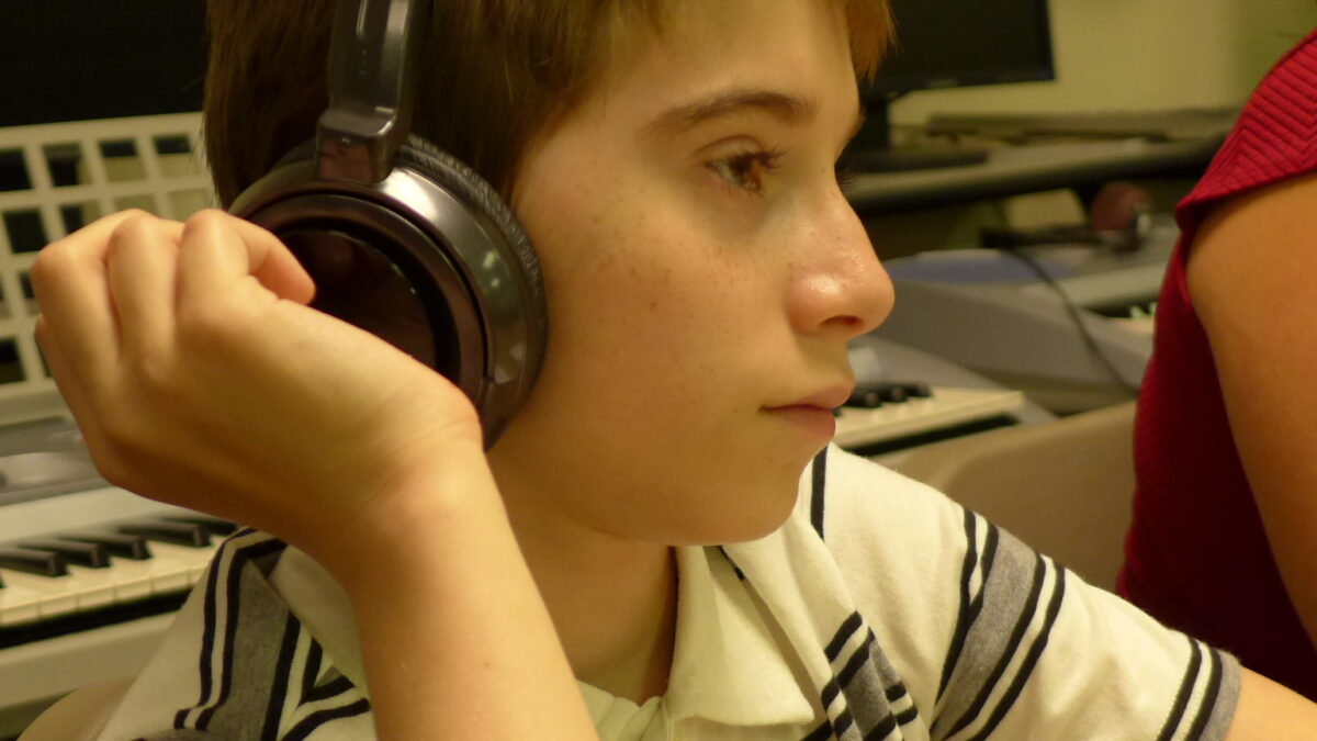 A youth wearing headphones sitting in front of computers