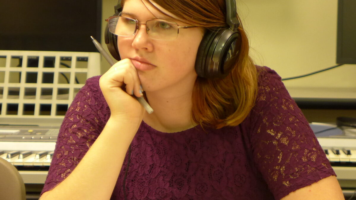 An individual wearing headphones holding a pencil sitting behind a piece of paper