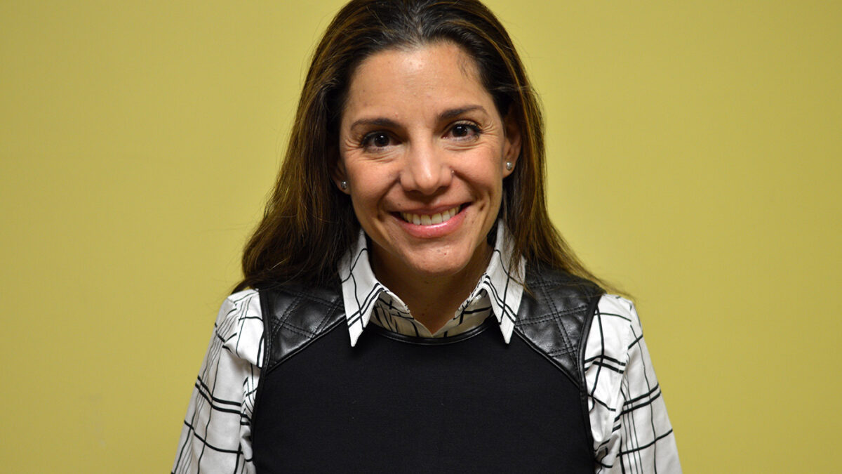 An adult wearing a black sweater vest over a black and white checkered shirt smiling in profile