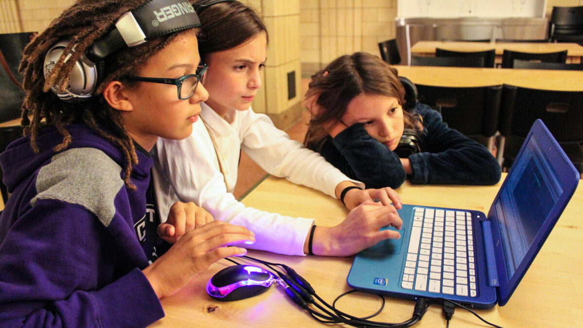 Three youth wearing headphones looking at a laptop