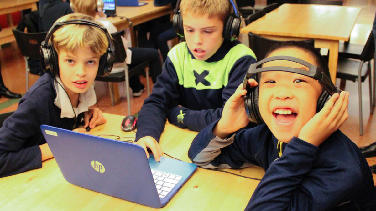 Three youth wearing headphones looking at a laptop