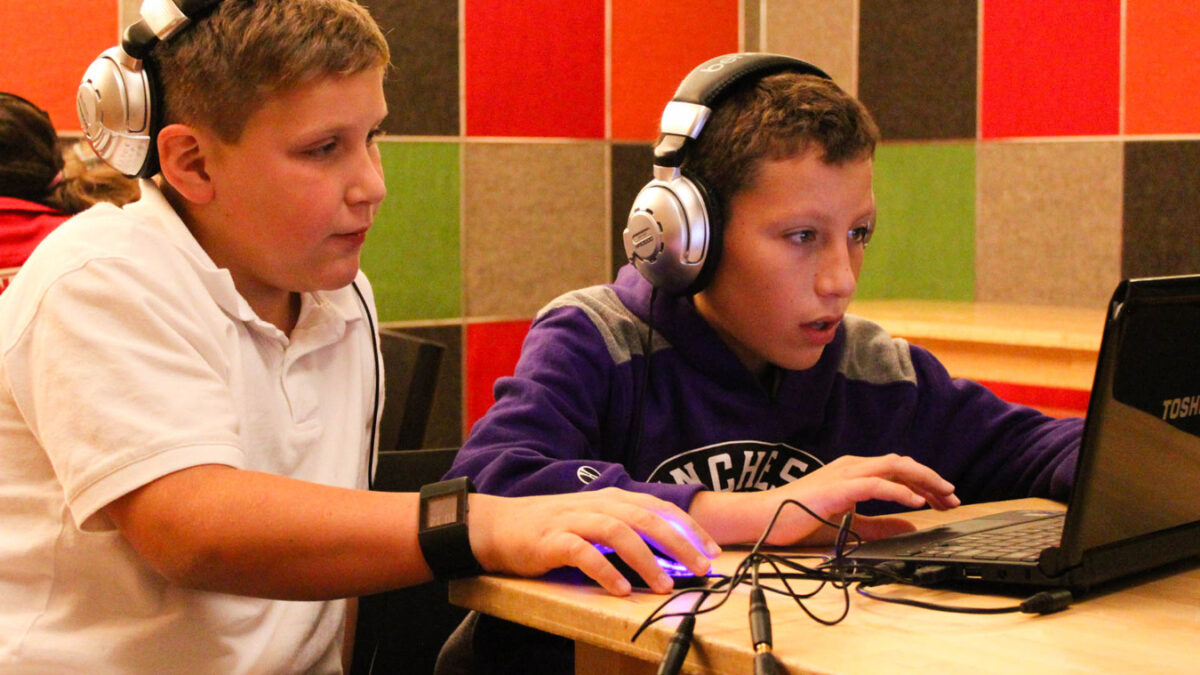 Two youth wearing headphones looking at a laptop