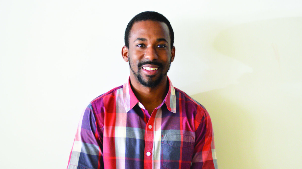 An adult wearing a red, white, and gray checkered shirt smiling in profile