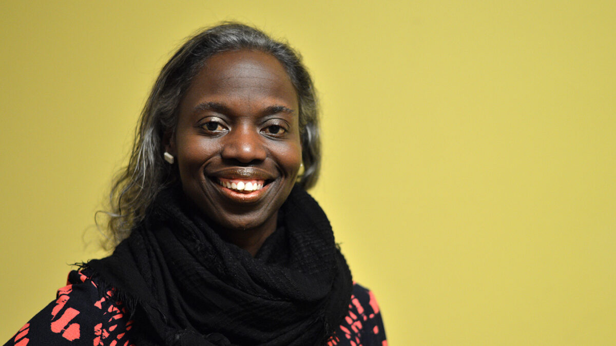 An adult wearing a black scarf and a red and black top smiling in profile