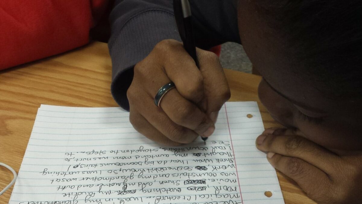 20151215_155712 A teen writing on a piece of notebook paper on a wooden table in a library