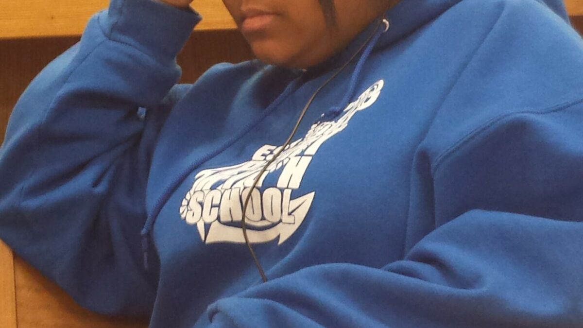 A teen wearing headphones sitting at a wooden table in a library