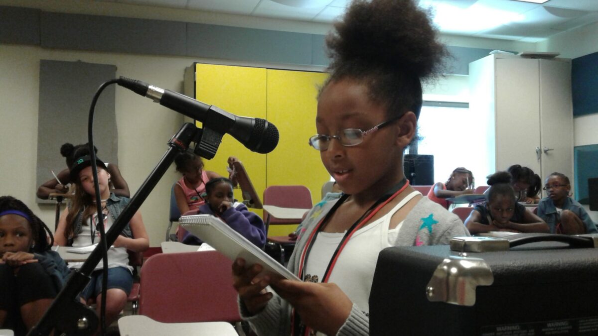 20160628_151323 A youth looking down at a notepad and speaking into a microphone in a classroom