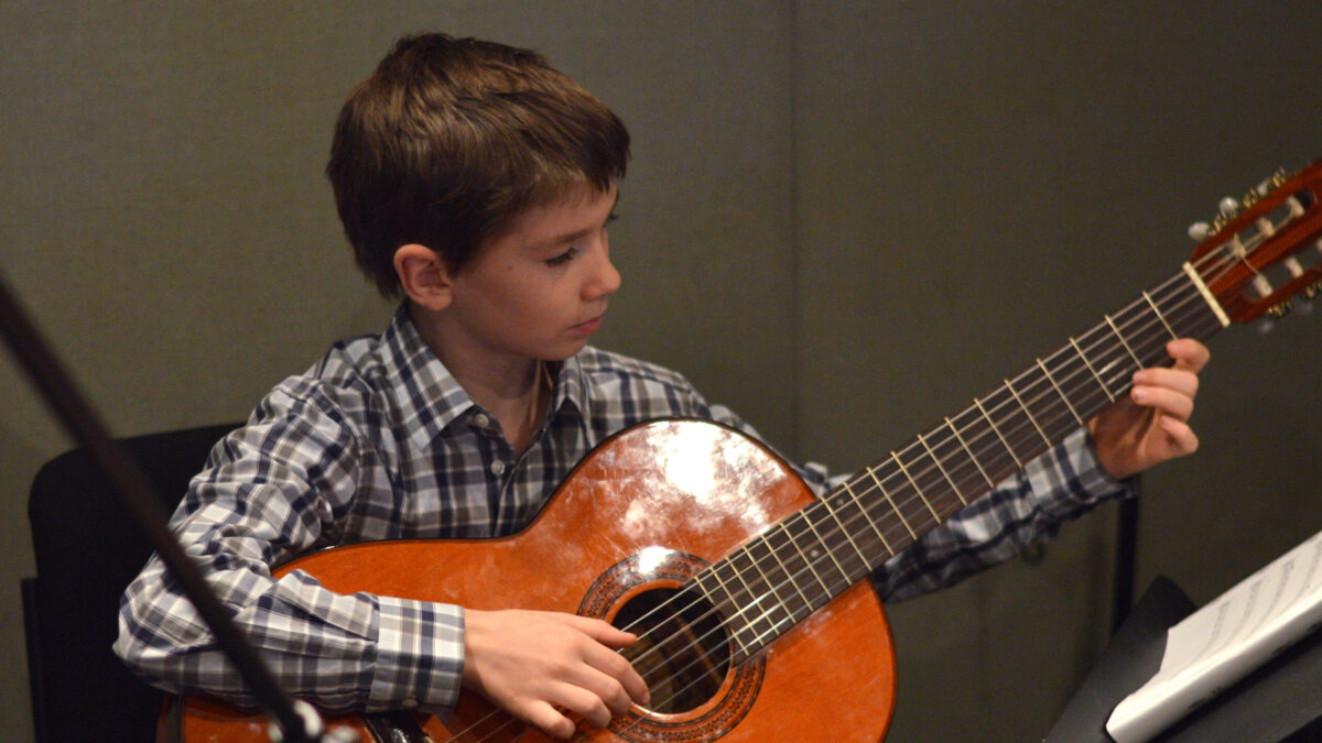 DSC_0007 A youth playing an acoustic guitar looking at sheet music on music stand in a radio studio