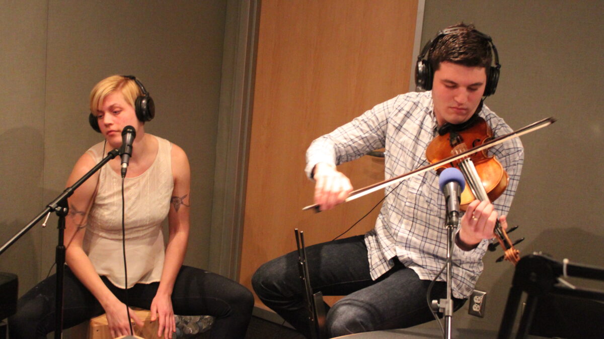 IMG_0631 An adult wearing headphones playing a cajon and an adult wearing headphones playing a violin in a radio studio