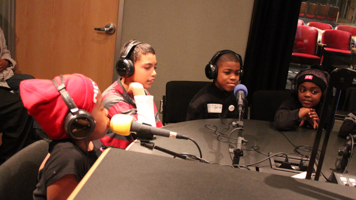 Four youth wearing headphones speaking into microphones in a radio studio