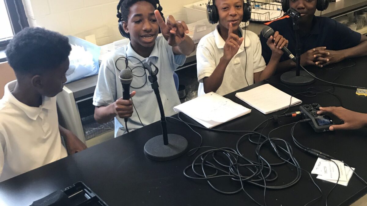 Four youth speaking into microphones, three wearing headphones