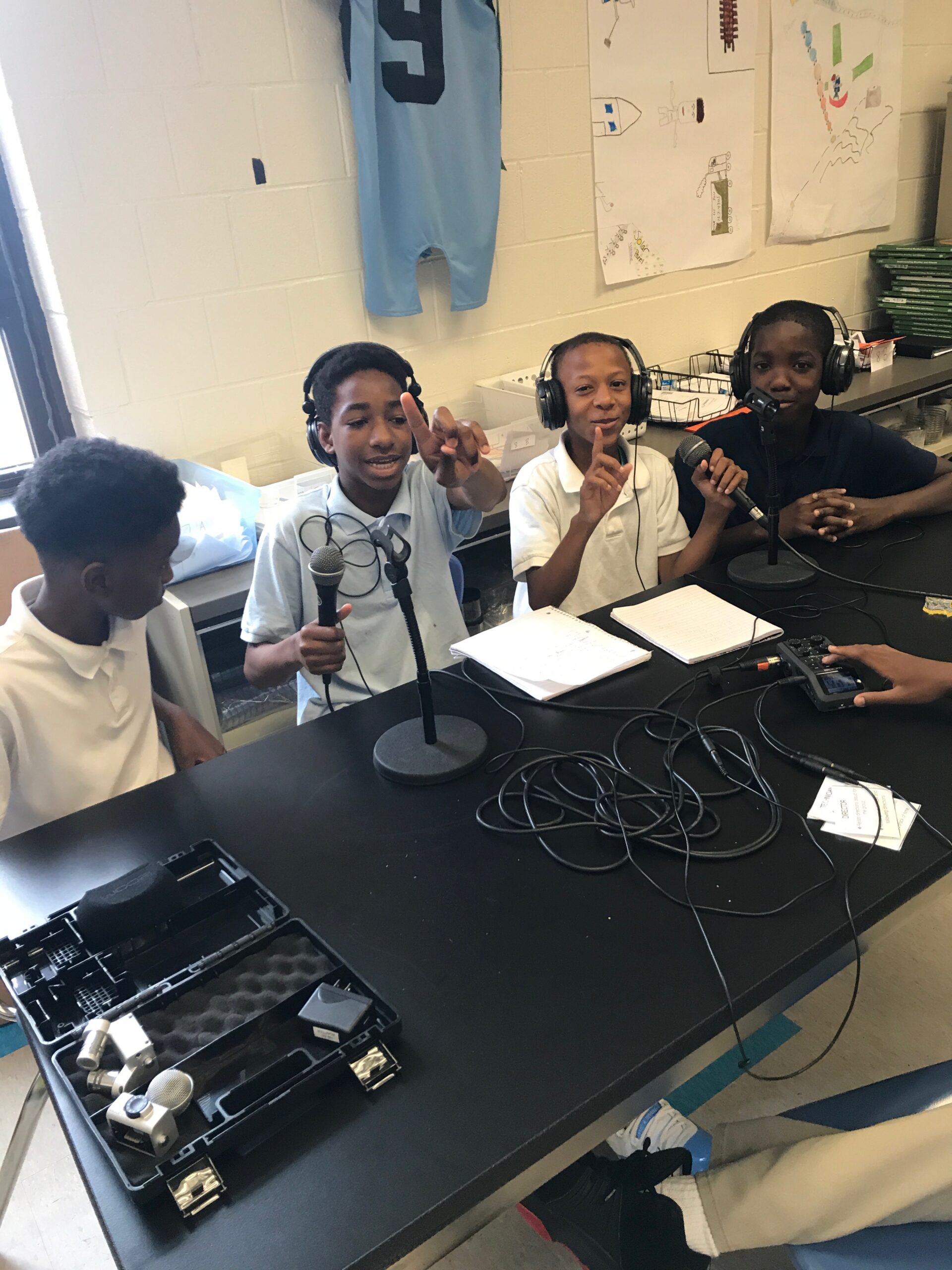 Four youth speaking into microphones, three wearing headphones