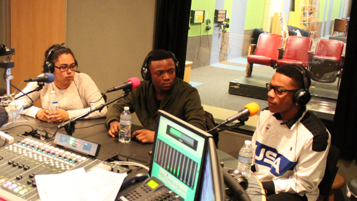 Three teens wearing headphones speaking into microphones in a radio studio