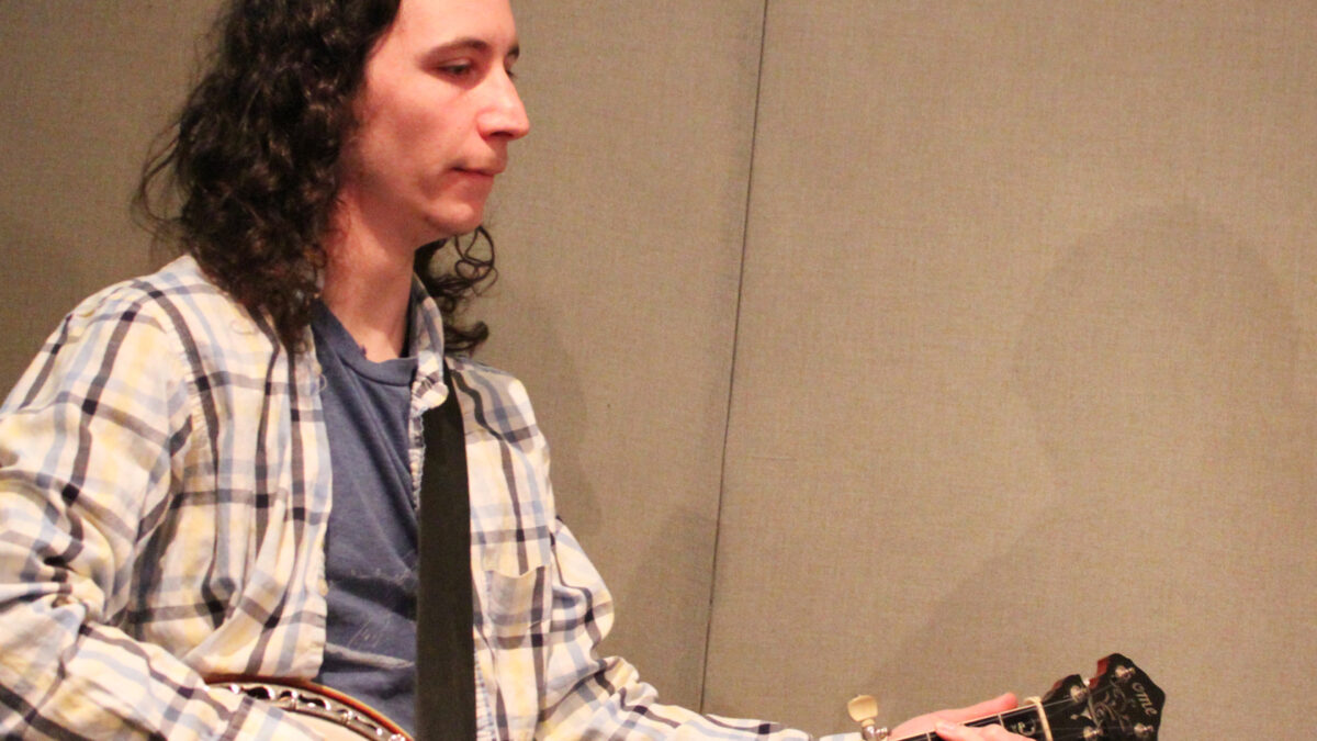 An adult playing banjo in a radio studio