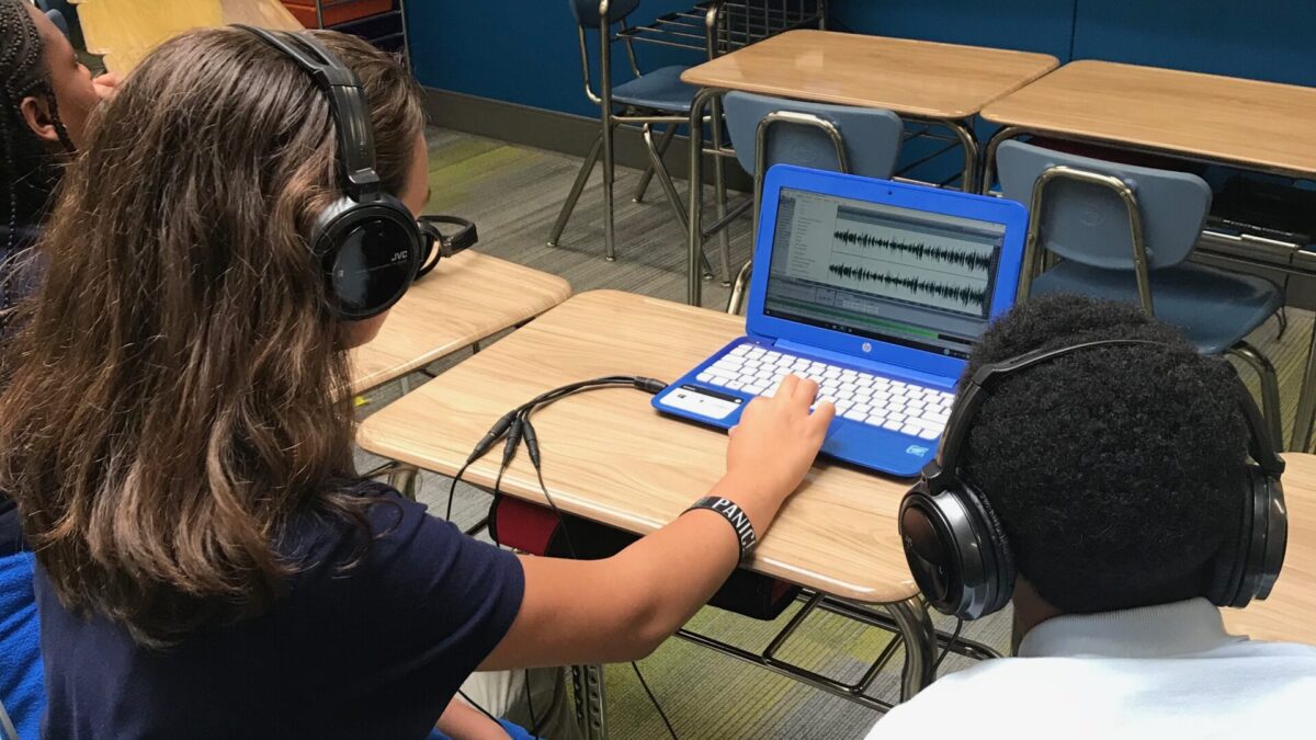Two youth wearing headphones looking at a blue laptop in a classroom
